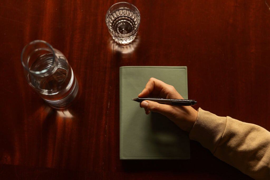 A hand writing in a journal at a wooden table